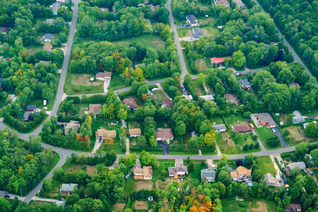 Aerial view of a green, tree-lined residential suburb in Ontario showing houses, driveways, and curved streets laid out under residential zoning by-laws, illustrating how Ontario zoning laws shape land use and neighborhood development patterns.