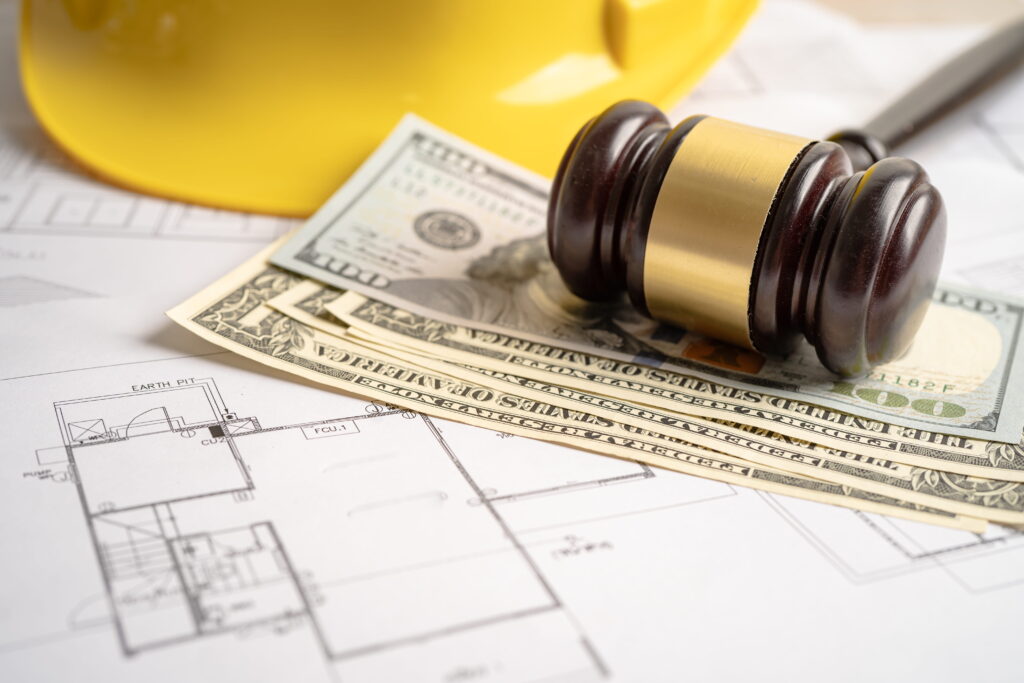 Architectural house blueprint with a judge's gavel, cash bills, and a yellow construction hard hat, representing building permit fees and legal requirements in Ontario.