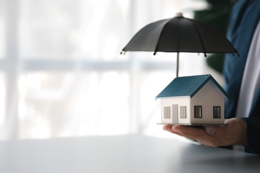 A hand holding a small model home protected by a miniature black umbrella, representing Tarion warranty insurance coverage for new homeowners against construction defects and builder failures in Ontario.