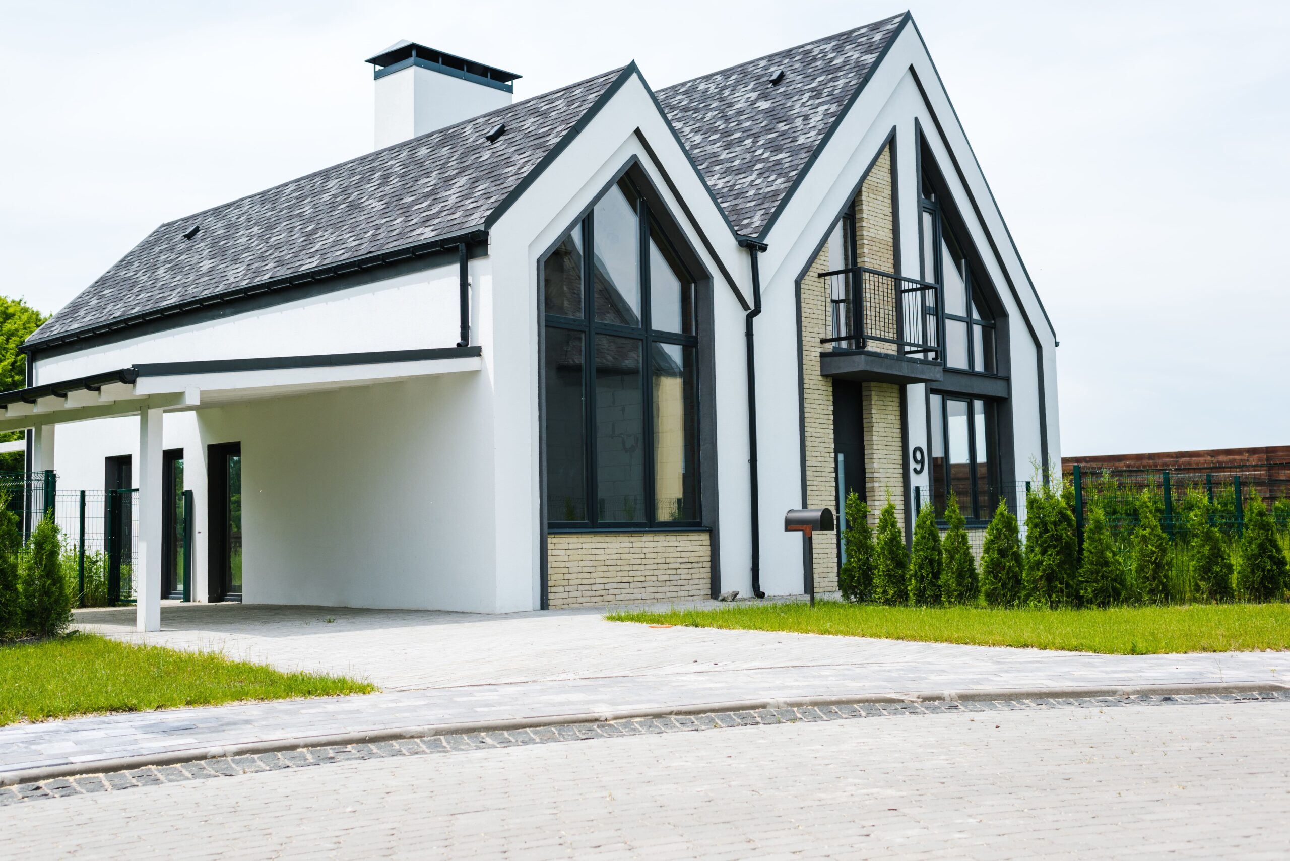 Exterior view of a newly completed modern custom home featuring large black-framed windows, white render, brick accents, and a landscaped front yard
