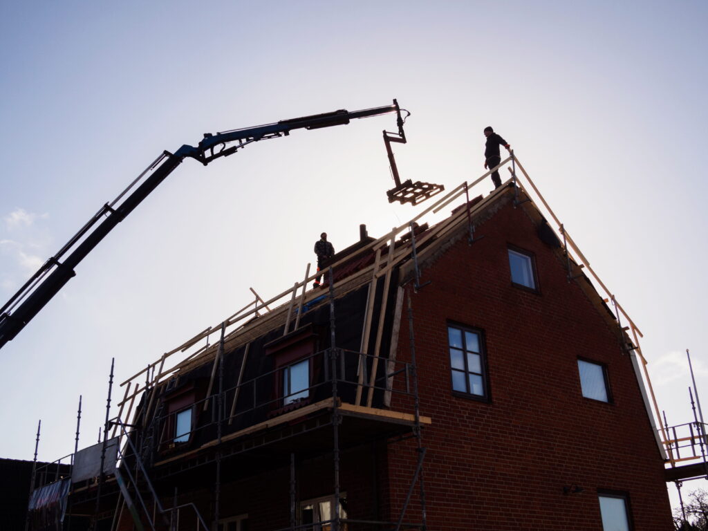 Construction workers and crane framing a second storey addition on a brick home, showing roof removal and upper floor build-out process in Ontario