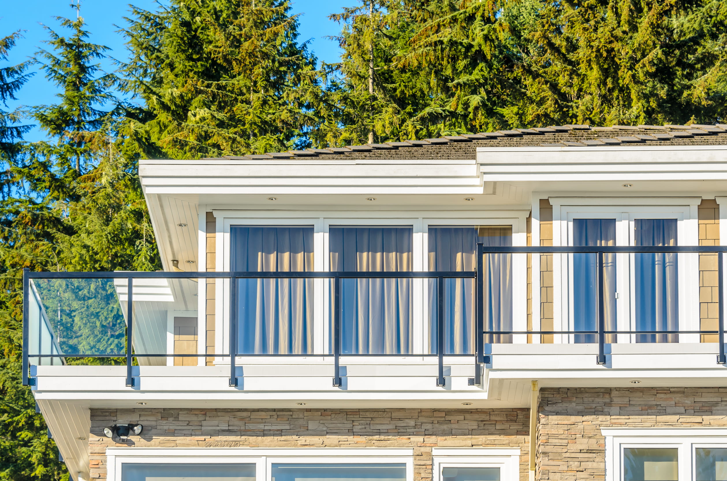 Completed second storey addition on an Ontario home featuring large windows, modern black metal balcony railing, and stone exterior finish