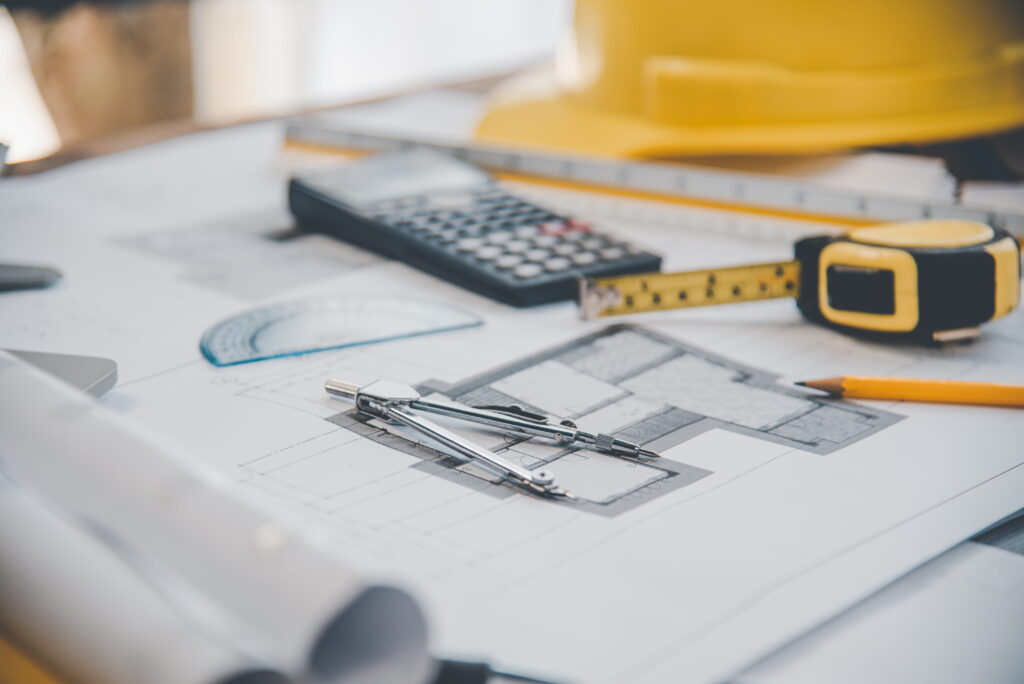 Construction site office with blueprints, white and yellow hard hats, and building plans pinned to wall — representing HCRA Ontario builder licensing and compliance planning